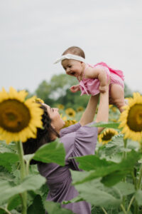 A mother tosses her infant daughter up for the camera at their Sunflower Field family session