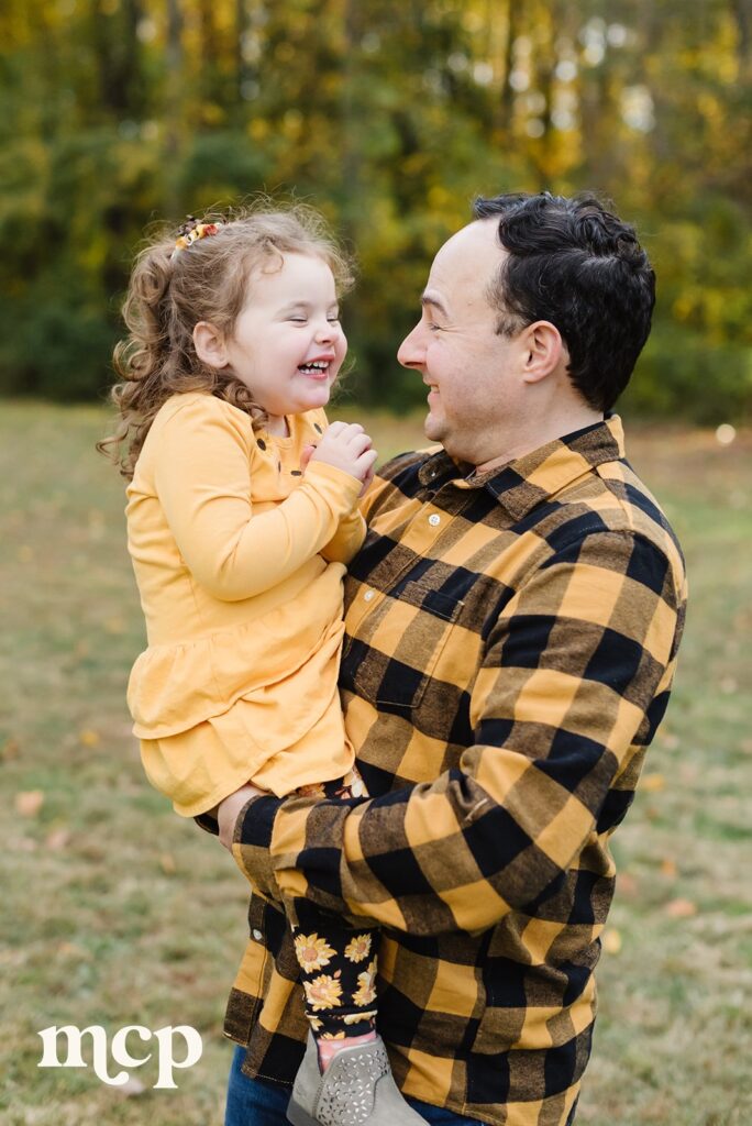 a young girl being held by her father giggles during her fall family portrait session