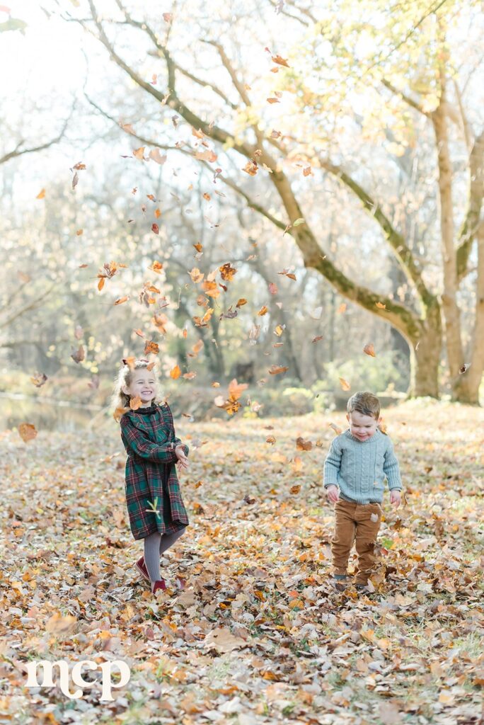 siblings play in the fallen leaves during their fall family portrait session